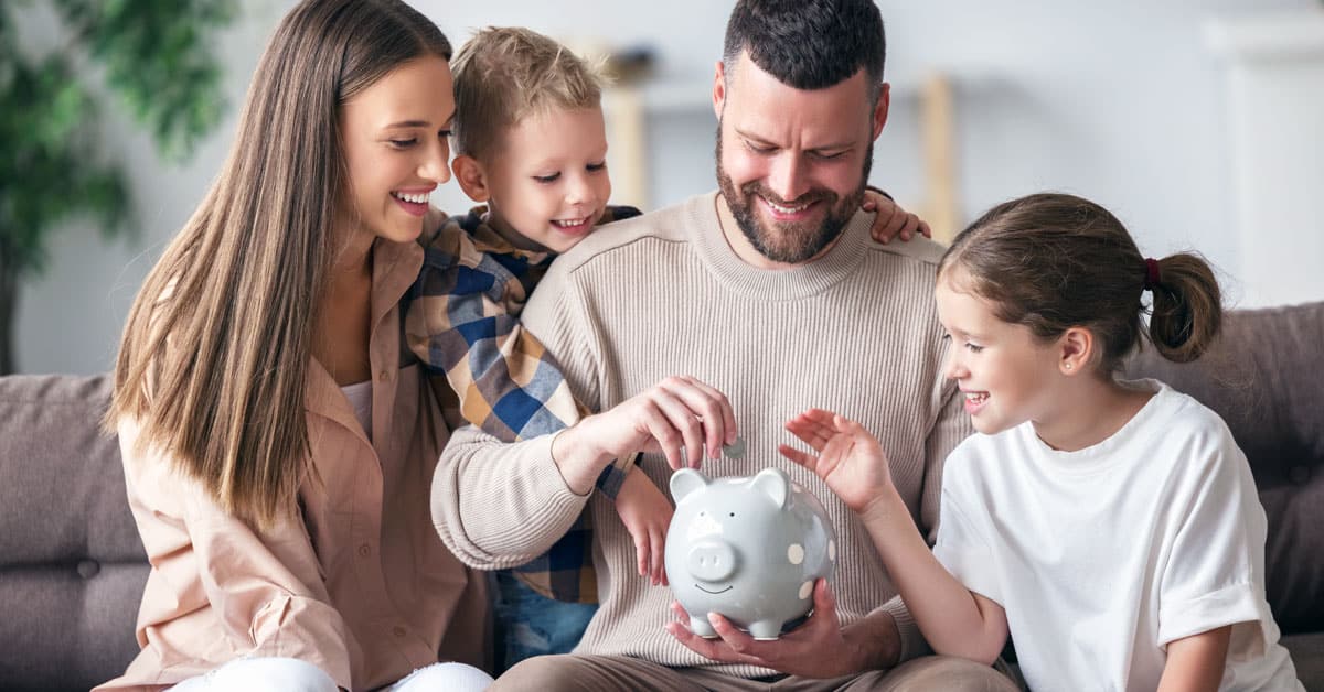 Family sitting on couch putting money into a piggy bank